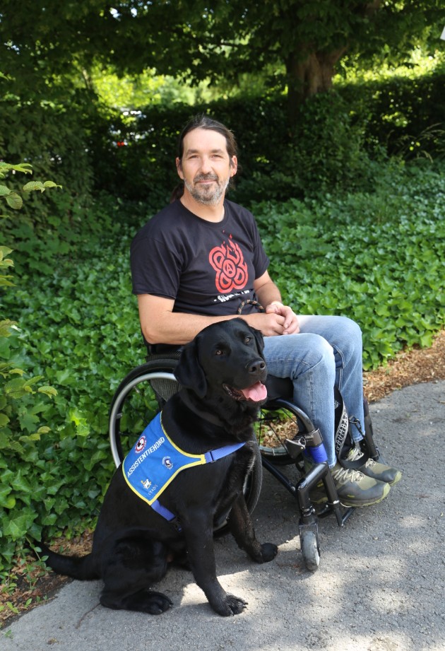 Man in rolstoel met assistentiehond aan zijn zijde, symbool voor de impact van gastgezinnen op iemands dagelijkse leven.
